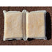 A white sponge pillow with two rectangular sections separated by a central indented seam, resting on a brown gravel surface. The pillow has a fibrous, mesh-like outer texture with a yellowish core visible through the material.